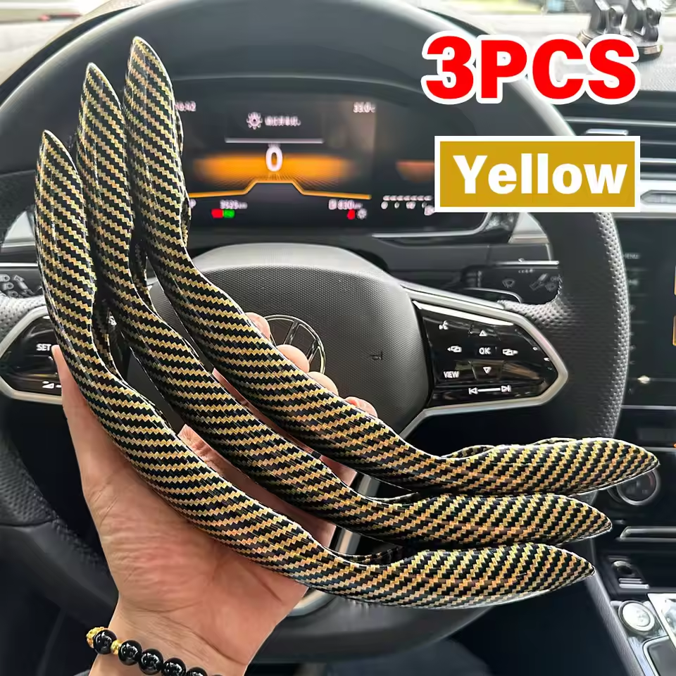 Three yellow carbon fiber steering wheel covers held in front of a car dashboard.
