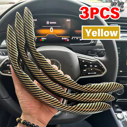 Three yellow carbon fiber steering wheel covers held in front of a car dashboard.